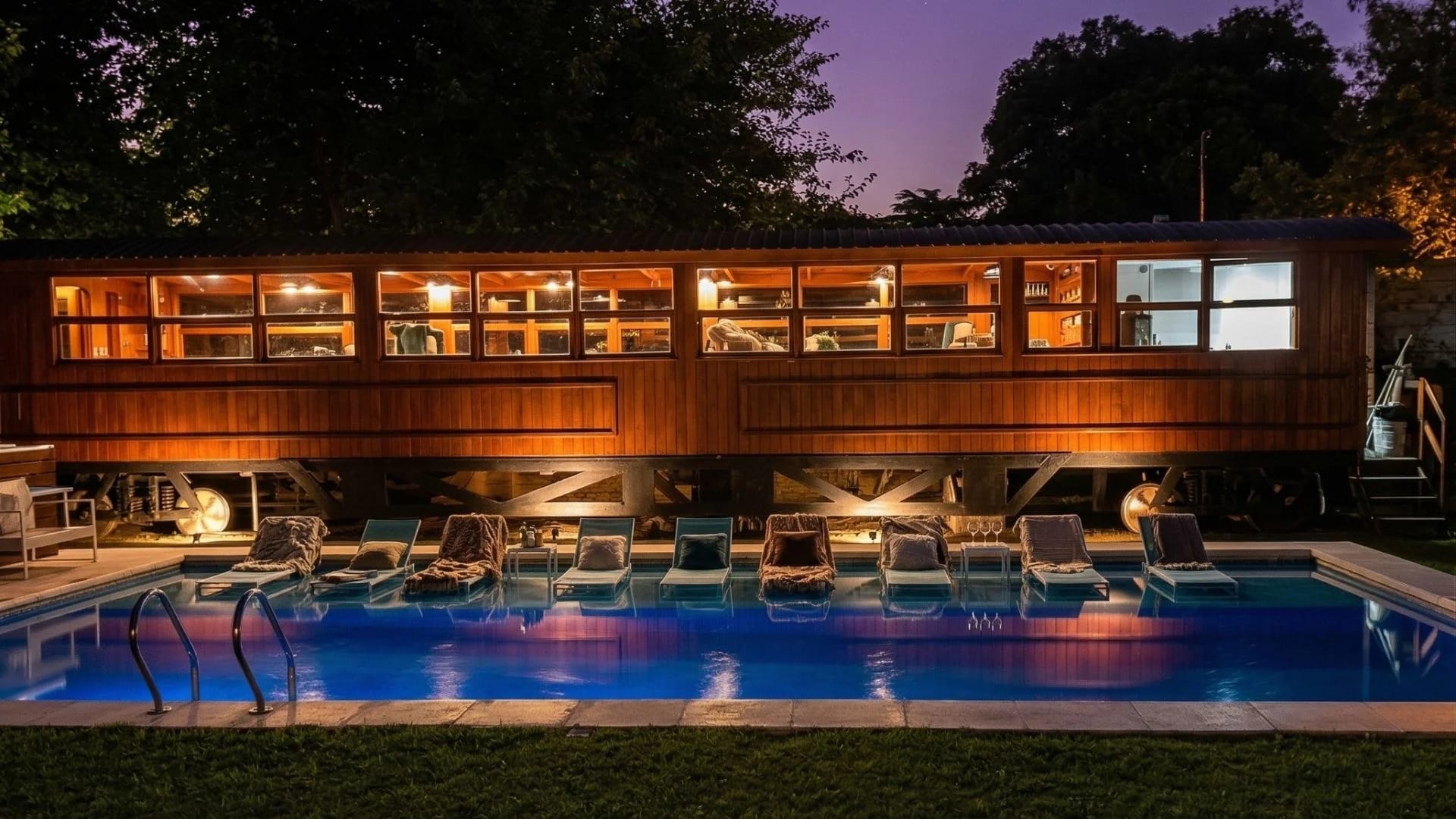 Vagón de tren restaurado como comedor, iluminado junto a la piscina